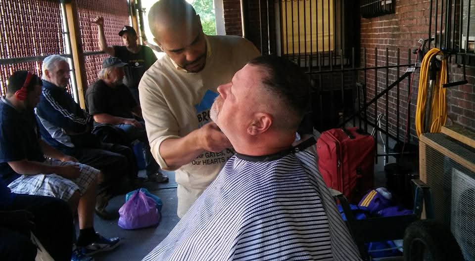 A Blessing by Barbers volunteer giving a free haircut on an outdoor porch