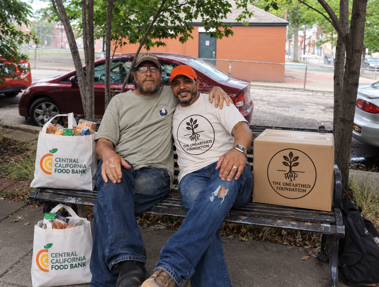 Two community members on a bench with Central California Food Bank bags and Unearthed Foundation food box